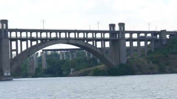 Zaporizhzhia, Ucrânia - 19 de junho de 2020: Barco de recreio turístico navega sob uma grande ponte de concreto velha perto de vista. - Filmagem, Vídeo