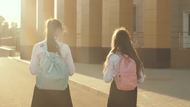 Девушки ходят в школу. Они очень веселятся. Школьницы с рюкзаками ходят в школу на улице. Концепция образования. здоровые подростки ходят на занятия на свежем воздухе. девочки болтают и разговаривают в школьном дворе - Кадры, видео
