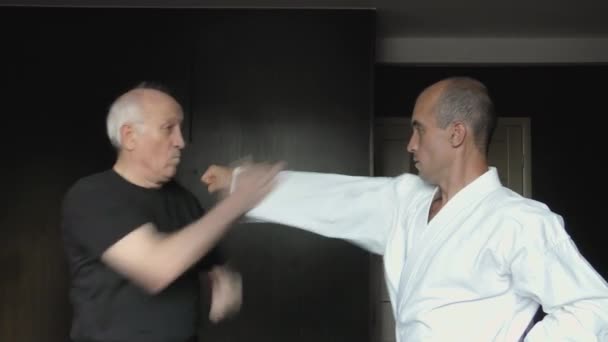 En una camiseta negra y karategi blanco, dos atletas entrenan puñetazos y bloques - Metraje, vídeo
