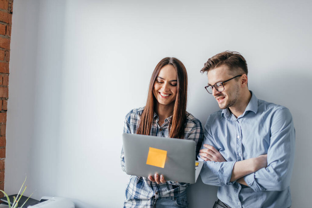 happy mix-race couple holding laptop computer while standing and celebrating isolated over gray wall background - Foto, Bild