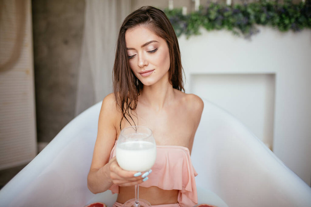Sensual attractive woman relaxing in bath with glass of milk. - 写真・画像