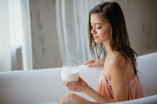 Zmysłowa atrakcyjna kobieta relaksująca się w kąpieli ze szklanką mleka. - Zdjęcie, obraz
