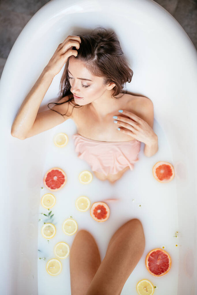 A young brunette woman takes a milk bath. - Фото, изображение