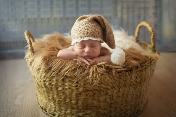 a small child in a basket sleeps in a warm knitted hat with a pompom - Foto, Imagem