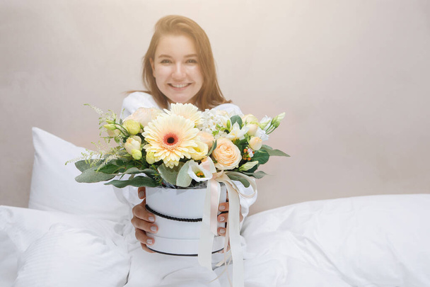 Genç bir kadın, sabah beyaz bir yatakta hediye olarak bir buket çiçek alır. Seçili odak. - Fotoğraf, Görsel