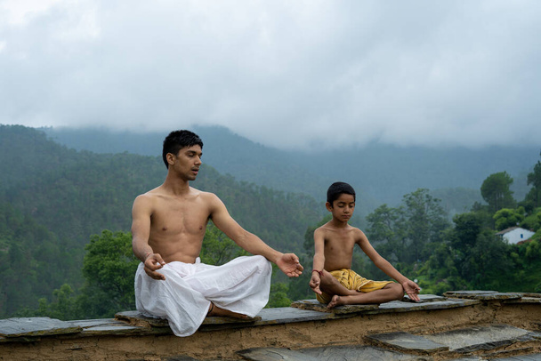 Un joven sentado en el techo con su hermano menor, ambos vistiendo dhoti, sonriendo a la cámara - Foto, Imagen