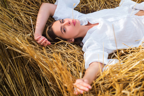 Young farmer woman while laying in hayloft. Sensual girl lying in the hay, haystack. Female portrait in field in countryside. - Foto, imagen