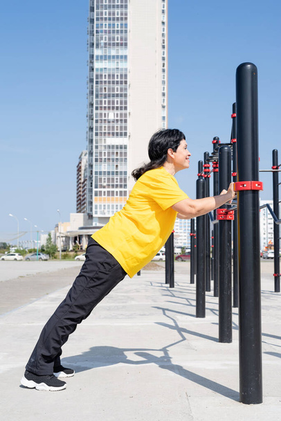 Smiling senior woman doing push ups outdoors on the sports ground bars - Photo, Image
