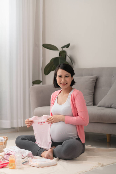 Gyönyörű terhes ázsiai nő csomagolás és előkészítés baba ruhák kosárban a várandós újszülött baba - Fotó, kép