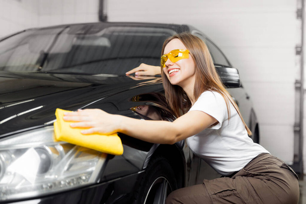 Car wash service, worker beautiful girl polishes and clean microfiber headlights on black auto - Valokuva, kuva