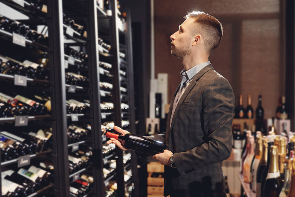 Sommelier takes bottle of red wine from counter of restaurant drinks store - Foto, Imagen