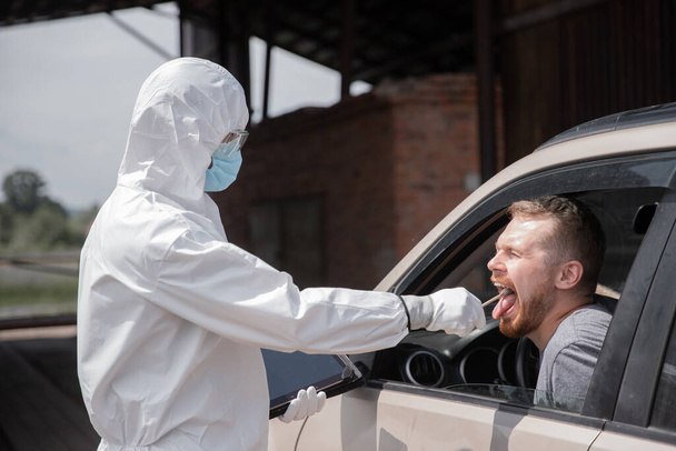 概念禁止運転者の車旅行のコロナウイルス。医者で保護ウイルススーツ取るスワブから男へテスト用COVID-19感染 - 写真・画像