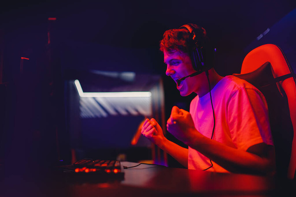 Gamer young man plays online video games computer and monitor wins tournament, rejoices and raises hands, neon color - Photo, Image