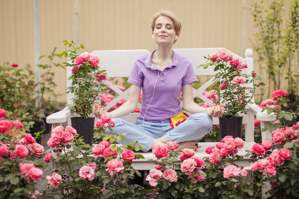 Beautiful young woman with short blond hair meditating roses in garden - Foto, Imagen