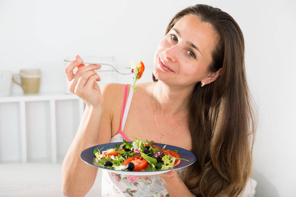 Positive pretty woman holding fork and eating vegetable salad in bed - Foto, afbeelding
