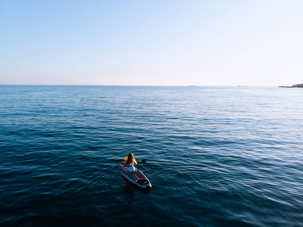 Attractive Woman on Stand Up Paddle Board, Woman paddling on sup board and enjoying turquoise transparent water. Tropical travel, wanderlust and water activity concept. Sunset and relax - Zdjęcie, obraz