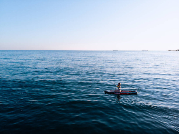 Attractive Woman on Stand Up Paddle Board, Woman paddling on sup board and enjoying turquoise transparent water. Tropical travel, wanderlust and water activity concept. Sunset and relax - 写真・画像