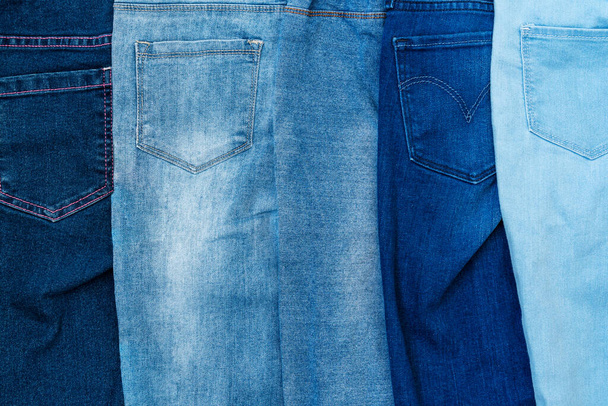 Textured background of a variety of denim pants in various shades of blue stacked in row - Фото, зображення