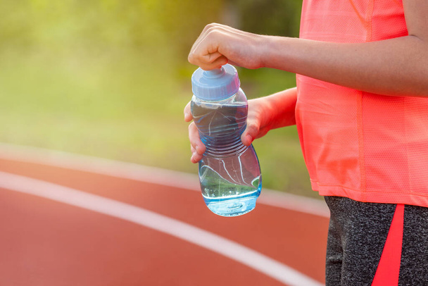Thirst and water balance concept. Girl holding bottle of water on running track on the stadium. - Foto, Imagem