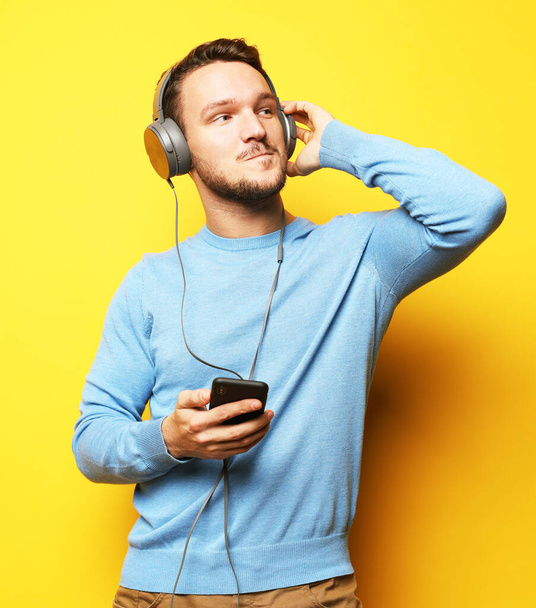 Handsome Man lictening to music over yellow background - Фото, изображение