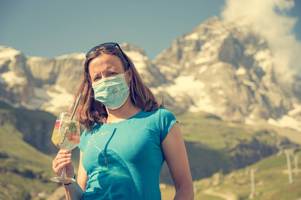 Femme heureuse tenant un verre à vin bénéficiant d'une vue sur la montagne tout en étant protégée par un masque facial. - Photo, image