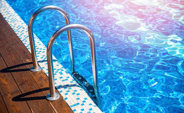 Blue swimming pool with grab ladder teak wood flooring stripes sunlight - Foto, Bild