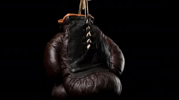 para skórzanych starych brązowych rękawiczek bokserskich wiszących na czarnym tle, zbliżenie - Materiał filmowy, wideo