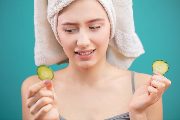 Woman with a towel on her head having fun, covering eyes with cucumber slices. - Foto, imagen
