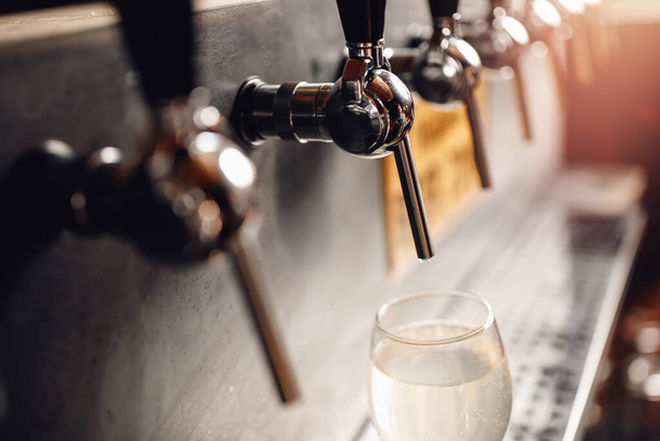 Dark background, Barman pours light alcoholic cider of keg tap into glass - Zdjęcie, obraz