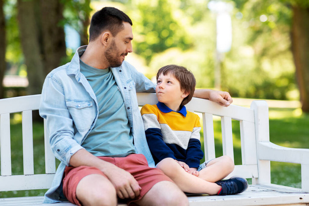 padre con hijo sentado en el banco del parque y hablando - Foto, Imagen