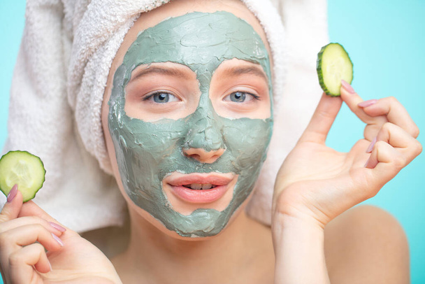 Positive smiling girl with clay cosmetic mask and organic cucumber slices - Fotó, kép