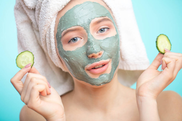 Skin care. Cheerful female with clay mask on face and cucumber slices - Фото, изображение