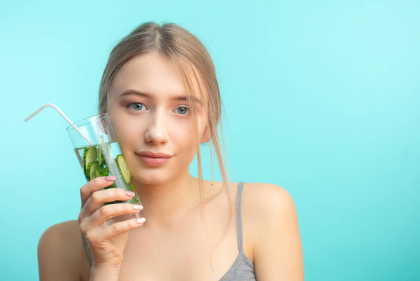 Spa woman with towel on head holding glass of cucumber water isoalted over blue - Photo, image