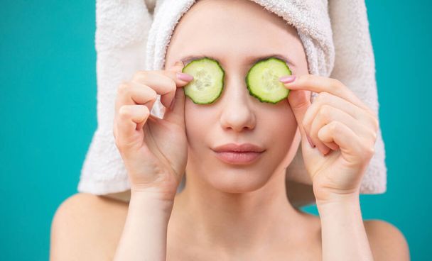 Woman with a towel on her head having fun, covering eyes with cucumber slices. - Photo, Image