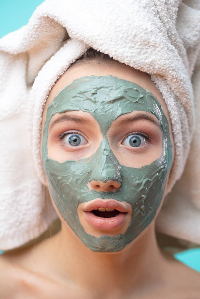 Macro shot of shoked surprised woman with clay facing mask and towel on face - Photo, image