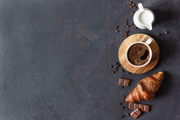 Kaffeetasse, Milch und Croissant auf schwarzem Hintergrund von oben mit Kopierraum. - Foto, Bild