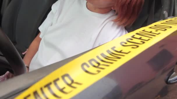 close up of forensic investigations underway with signs on scientific evidence and yellow police tape at a fake female corpse leaning against the window of her car - Filmagem, Vídeo