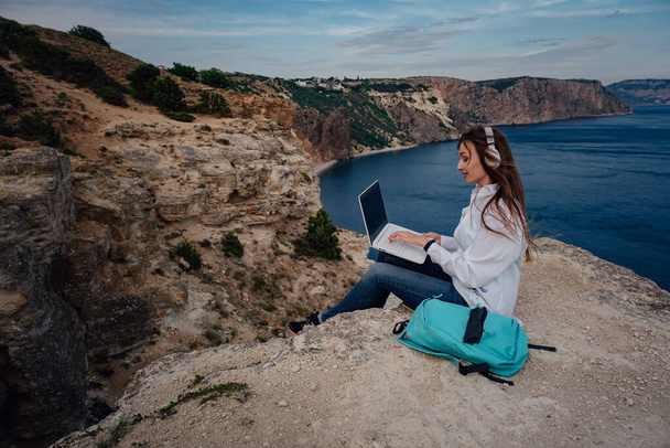 Junge Geschäftsfrau am Computer am Strand an der Felswand. Technologie und Reisen. Arbeiten im Freien. Freiberufliches Konzept. - Foto, Bild