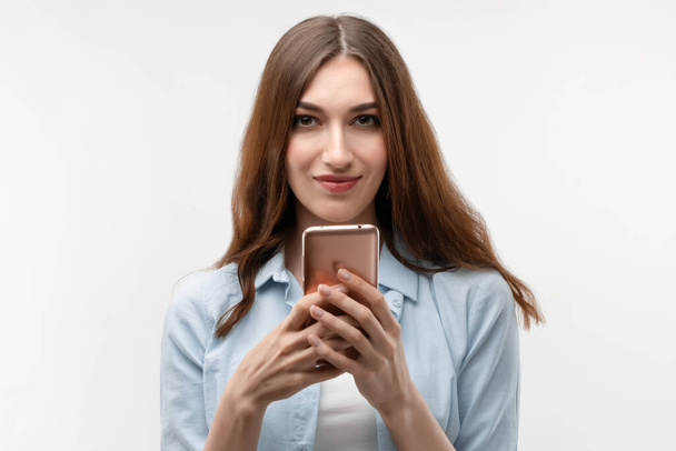 Happy Young woman with long chestnut hair, dressed in casual clothes, using smartphone on white background. New useful application. - Zdjęcie, obraz