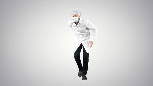 Doctor wearing his uniform and wearing a mask he is walking in a funny way on gradient background. - 写真・画像