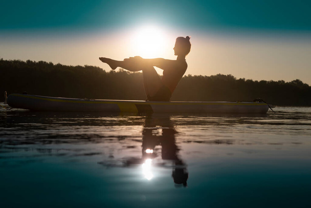 Mujer meditando y practicando yoga durante el amanecer en paddle board - Foto, Imagen