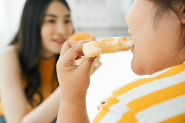 Primer plano de asiático gordito mujer comer dulce donut para el almuerzo. Comida chatarra poco saludable. - Foto, imagen