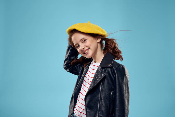 Siyah ceketli, kafasında sarı şapkalı, kızıl saçlı, mavi arka planlı güzel bir kız. - Fotoğraf, Görsel
