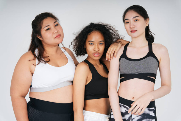 Group of three diverse women with asian and african in sport bra outfit over white background. - Photo, Image