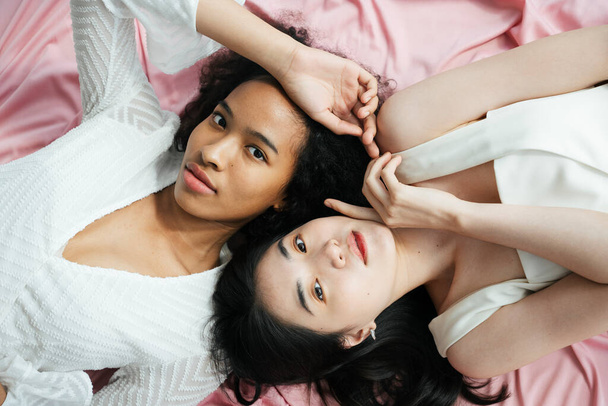 Top view - Asian and african women in white shirt laying on pink cloth. - Valokuva, kuva