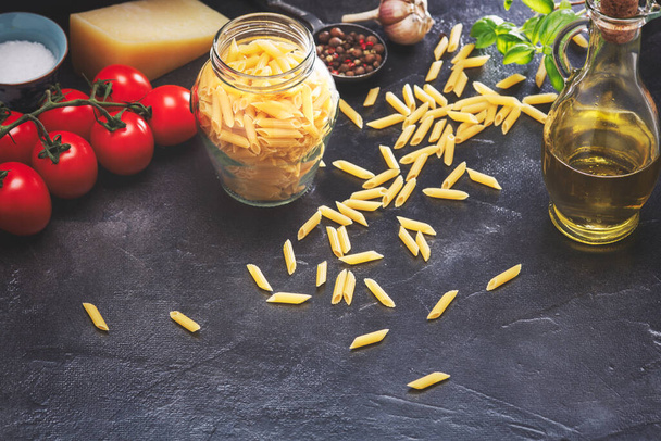Italiaanse pasta mini penne rigate, olijfolie, verse tomaten, parmezaanse kaas en specerijen op tafel - Foto, afbeelding