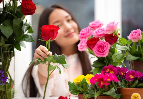 Kırmızı ve pembe gülleri budamaya hazırlanan kadın ve evdeki güzel çiçek aranjmanları Sevgililer Günü için vazoyla çiçek aranjmanları ve masada aile içi hediyeler. - Fotoğraf, Görsel