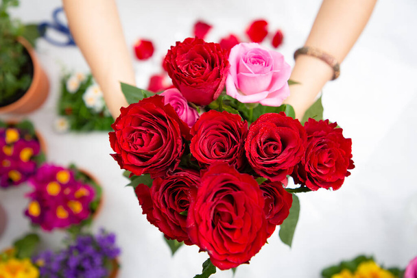 Žena Příprava na zdobení červené a růžové růže a krásné květinové aranžmá v domácnosti, květinové aranžmá s vázou pro dárkové dárky na Valentýna a podnikání v rodině na stole - Fotografie, Obrázek