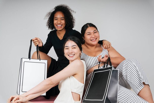 Retrato de grupo de tres mujeres diversas con asiática y africana sosteniendo bolsas de compras para maqueta sobre fondo blanco. - Foto, imagen