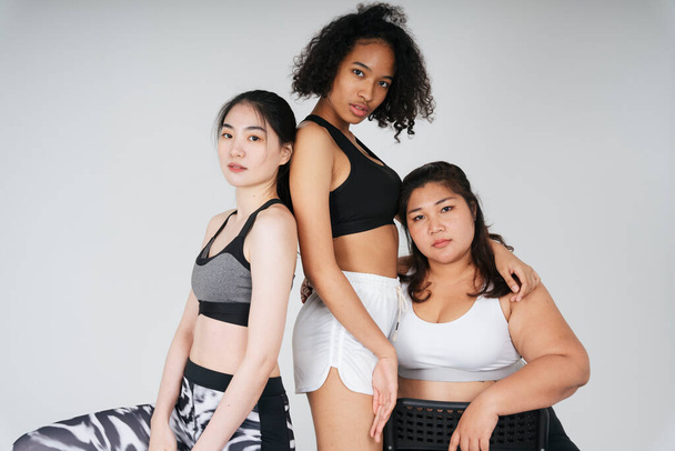 アジア系とアフリカ系の3人の女性のグループは、白い背景にスポーツブラジャーの衣装で. - 写真・画像